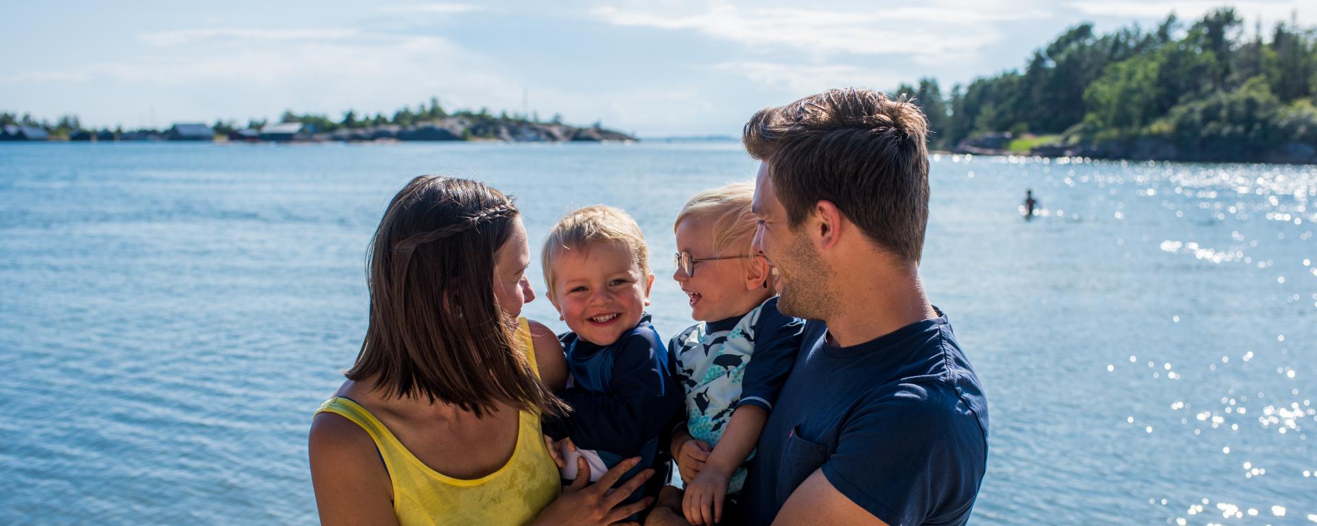 Par med två små barn på strand på Åland med havet i bakgrunden.
