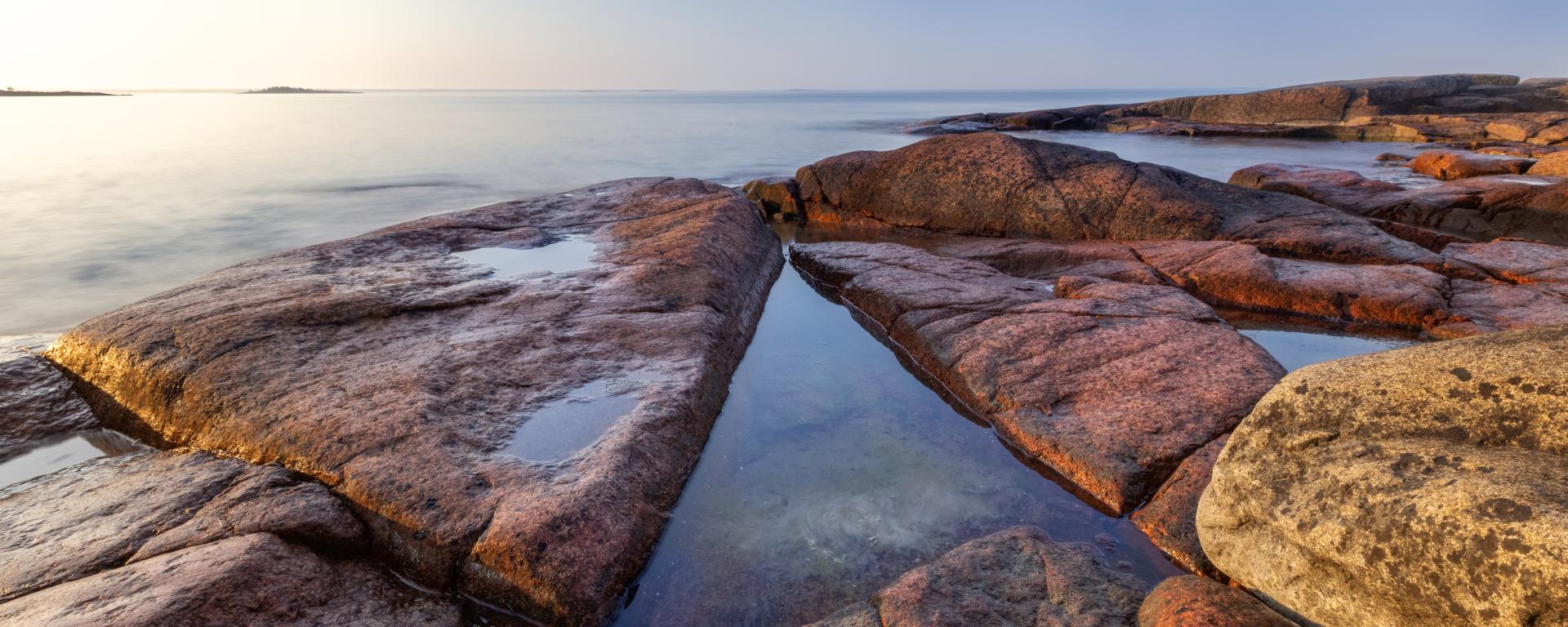 Vacker tidig solig morgon på granitröda klippor vid blankt hav på Åland.