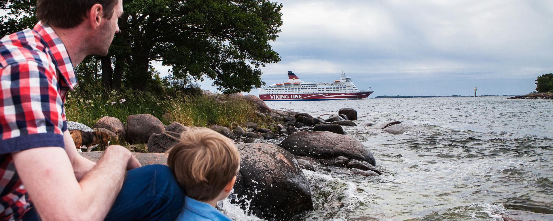 Pappa med barn tittar på när Viking Lines fartyg passerar stranden.