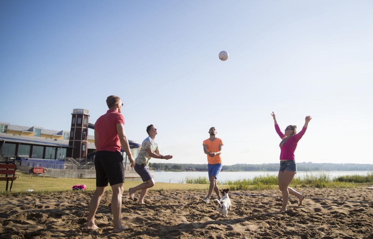Unga vuxna spelar beachvolleyboll på stranden.