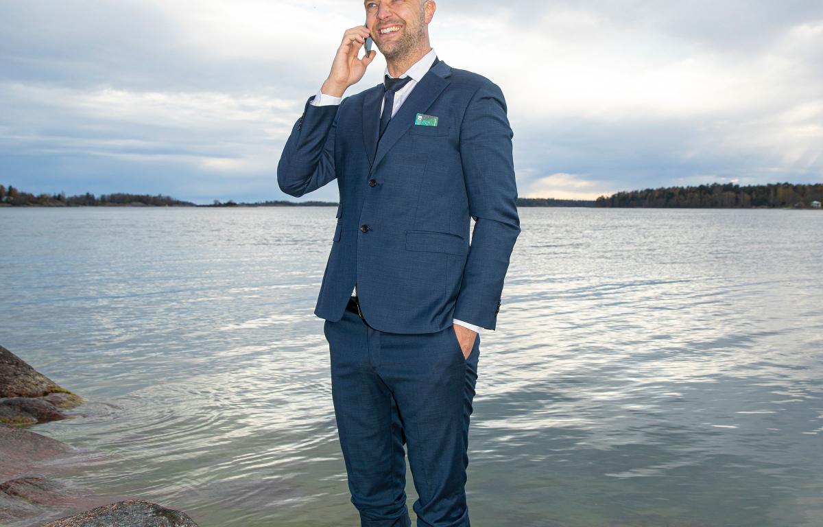 Man i kostym står i vattnet vid strandkanten och pratar i telefon.