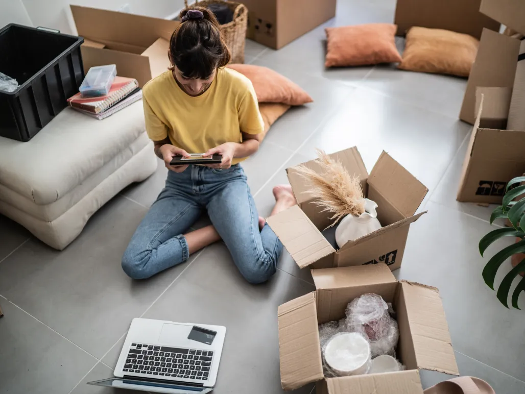 Ung kvinna sitter på golvet i nya lägenheten omgiven av flyttlådor.
